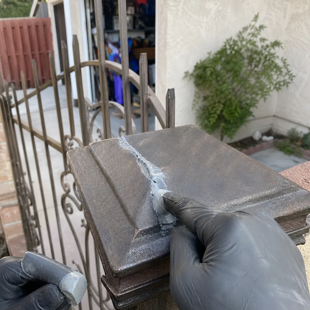 Professional repairing a cracked metal post cap on an ornamental gate